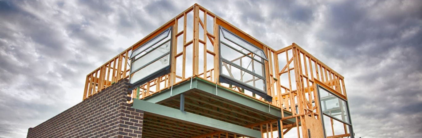 Structure of half-built house showing timber frame and bricks against a cloudy sky