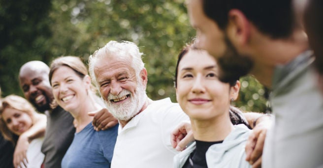 Line of people of mixed genders, cultures and ages with their arms around each other's shoulders smiling